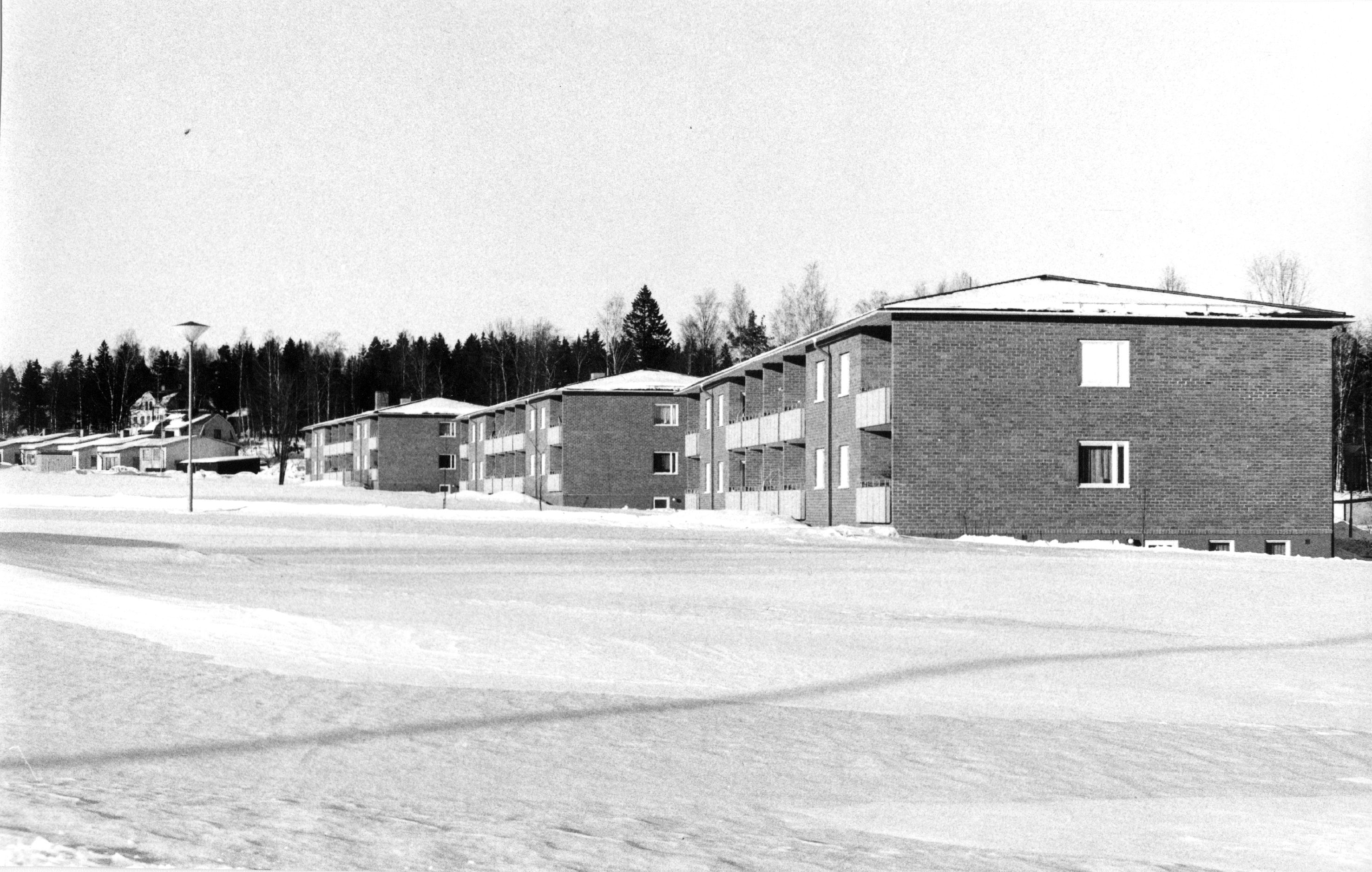 En svartvit vinterbild med tre tvåvåningshus.