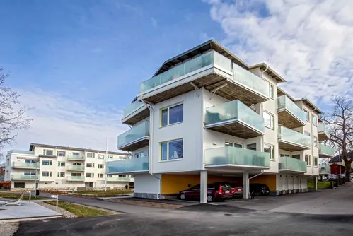 Bilden föreställer ett vitt flerfamiljshus med balkongräcken i glas.